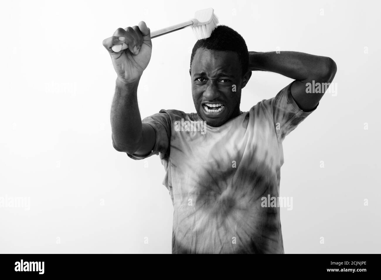 Studioaufnahme eines jungen schwarzen afrikanischen Mannes mit Reinigungsbürste Um sein Haar vor weißem Hintergrund zu waschen Stockfoto
