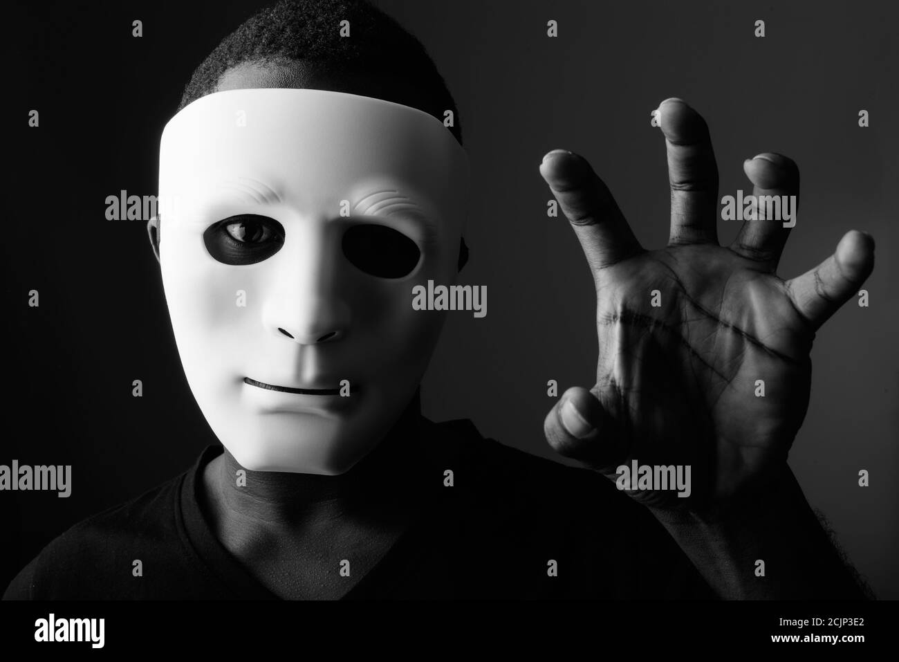 Studioaufnahme eines jungen schwarzen afrikanischen Mannes im dunklen Raum Mit Maske und zeigt seine Hand Stockfoto