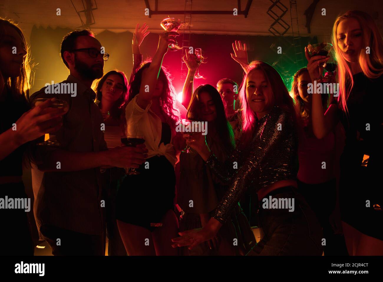 Emotionen. Eine Menge von Menschen in Silhouette hebt die Hände und tanzt auf Tanzfläche auf neonhellem Hintergrund. Nachtleben, Club, Musik, Tanz, Bewegung, Jugend. Helle Farben und bewegende Mädchen und Jungen. Stockfoto