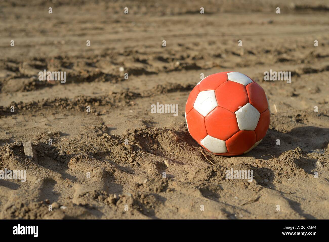 Gebrauchte Fußball in rot und weiß auf schmutzigsten Erde Stockfoto