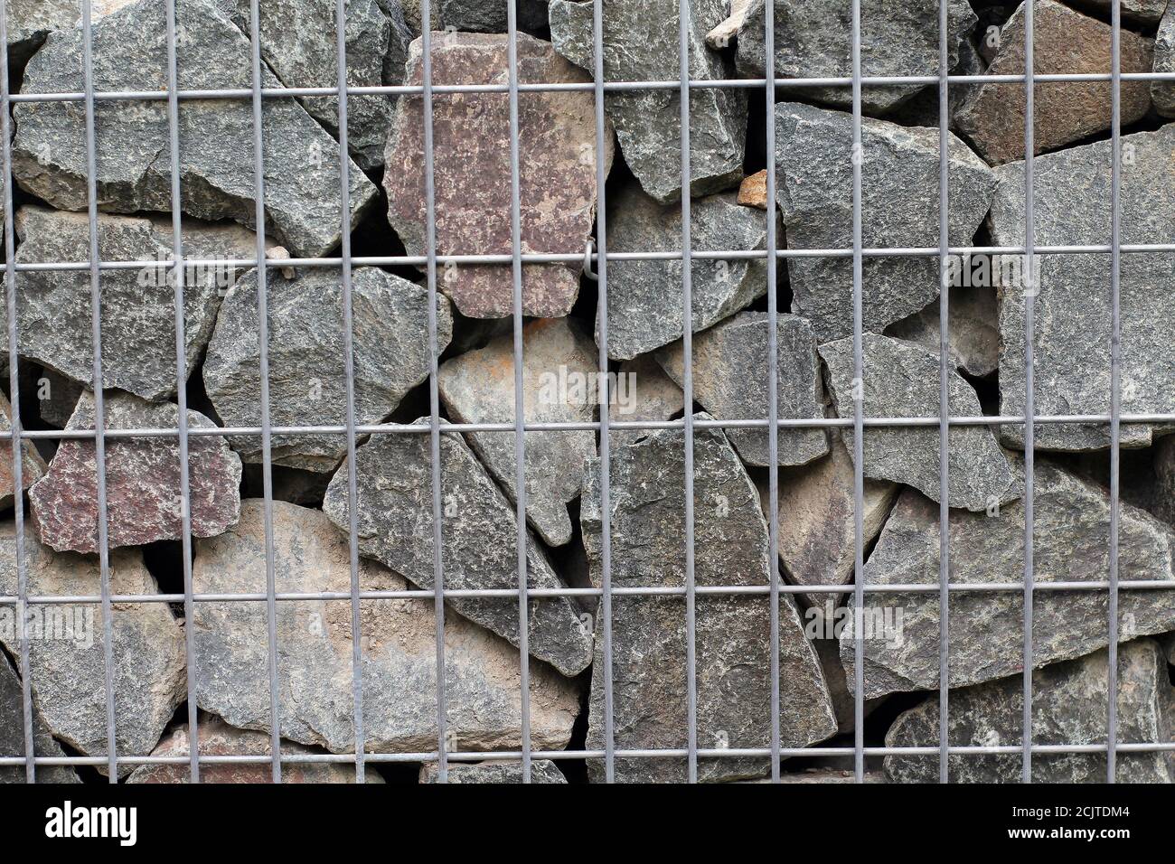 Gestapelte Pflastersteine, mit Stahlgeflecht fixiert. Wand aus Steinen unter Metallgitter. Stockfoto