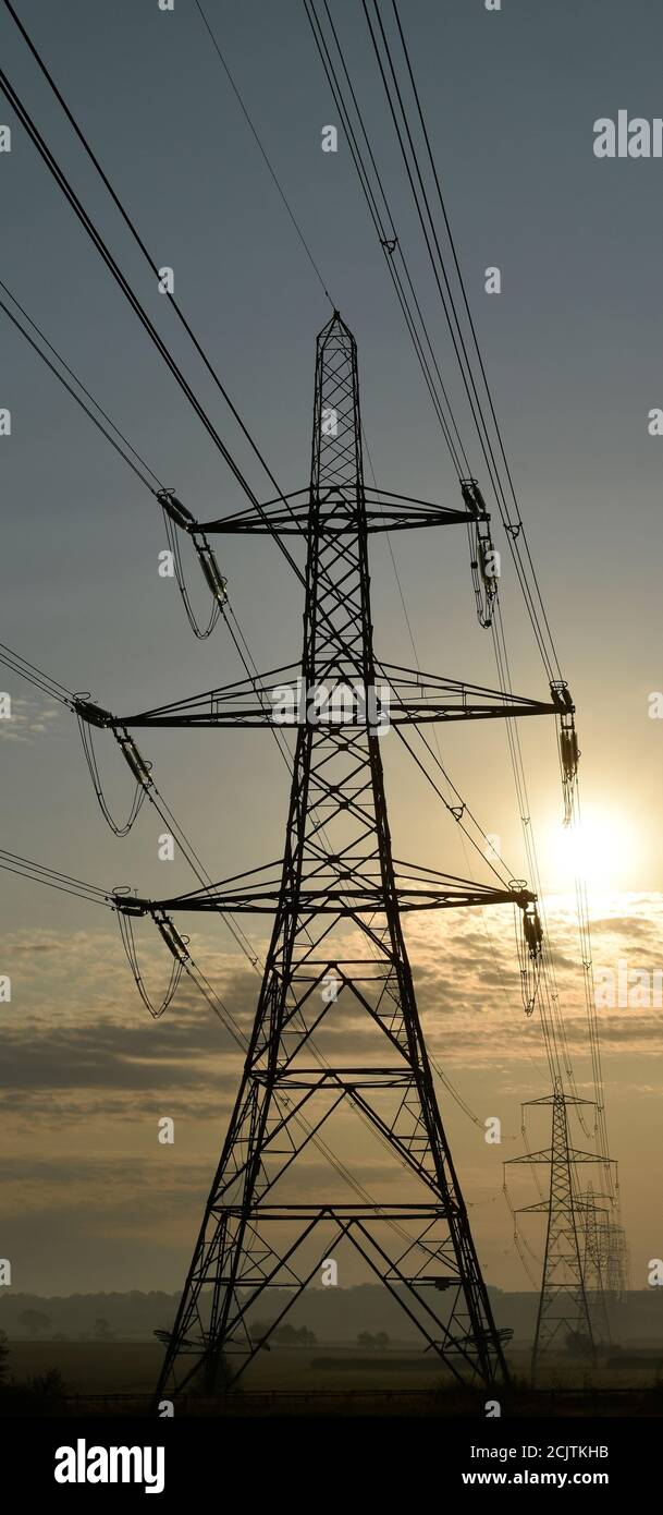 National Grid Strom Masten in einer Reihe zu Horizont Silhouette bei Sonnenaufgang. Stockfoto