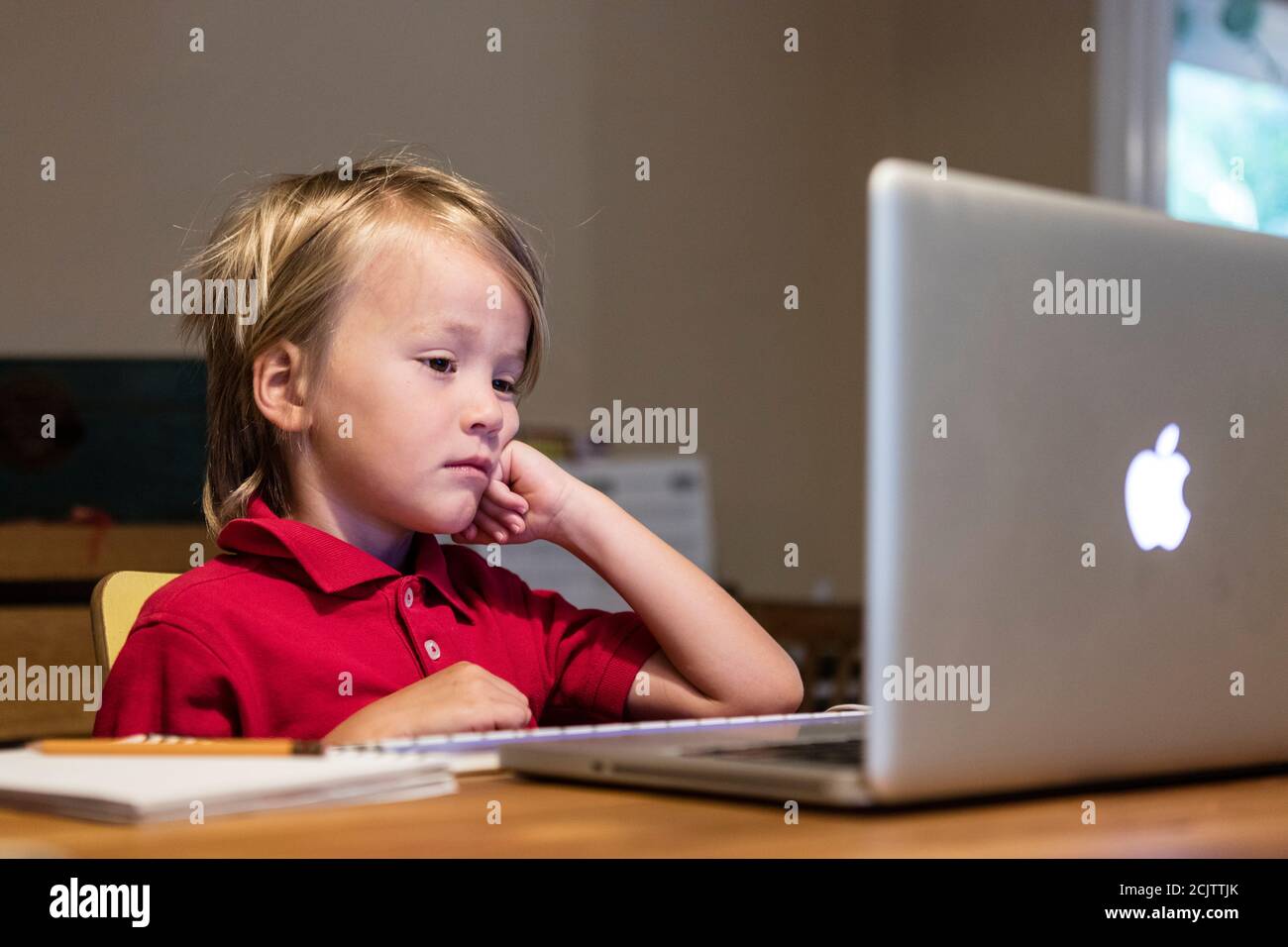 Ein kleiner Junge sieht gelangweilt aus, während er zuhause am Esstisch sitzt, in Miami, Florida, USA Stockfoto