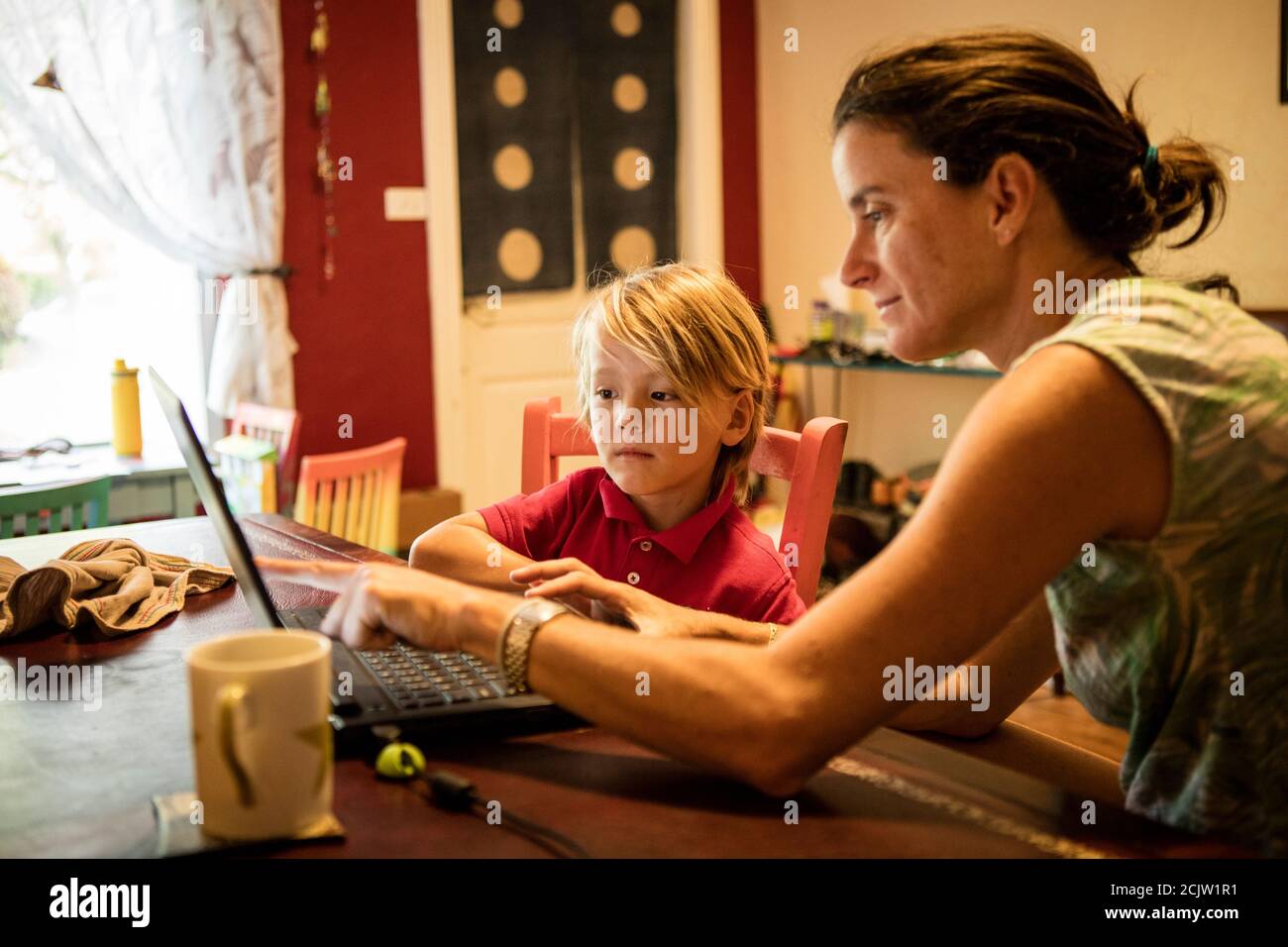 Eine Mutter hilft ihrem kleinen Sohn vor einem Laptop, während sie Fernunterricht an einem Tisch zu Hause in Miami, Florida, USA, macht Stockfoto