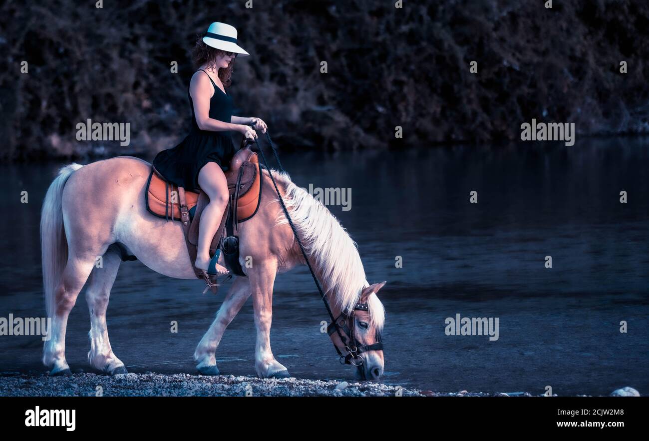 Cowgirl Frau wässert ihr Pferd in einem Fluss. Teen Mädchen auf einem Pferd im Wasser. Stockfoto