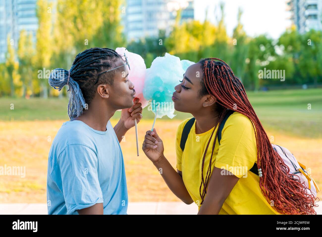 Ein glückliches schwarzes Paar, das bunte Zuckerwatte zusammen in einem Park einer großen Stadt hat. Stockfoto