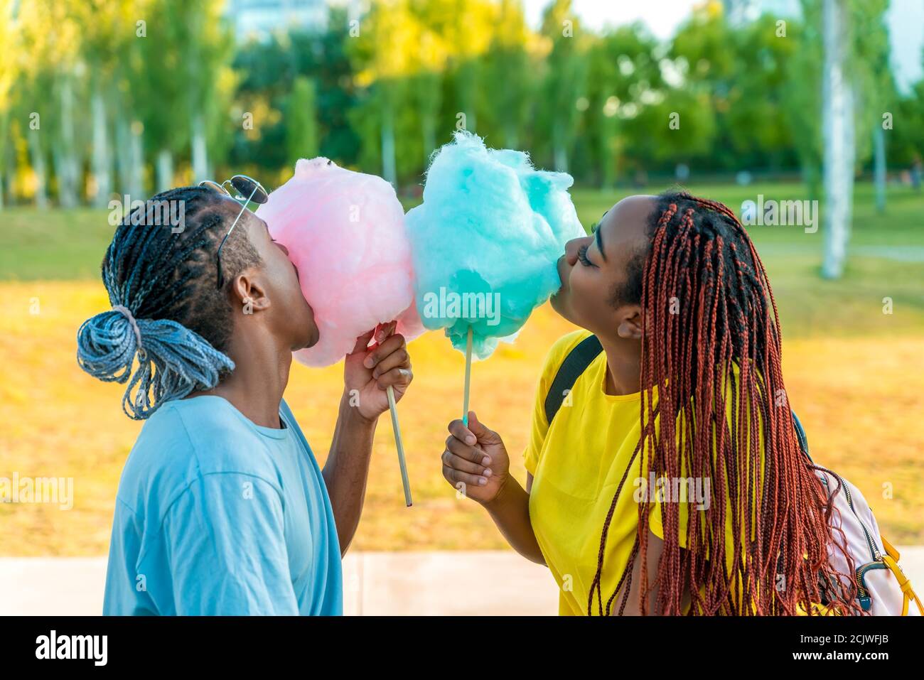 Ein glückliches schwarzes Paar, das bunte Zuckerwatte zusammen in einem Park einer großen Stadt hat. Stockfoto