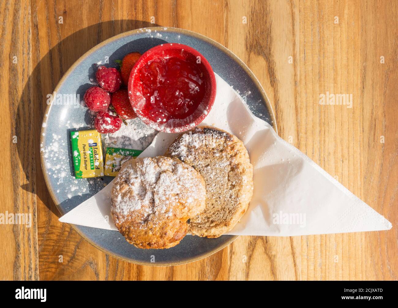 Ein Fruchtkegel mit frischem Obst, Marmelade und Pats Butter auf einem Teller vor einem Holzhintergrund Stockfoto