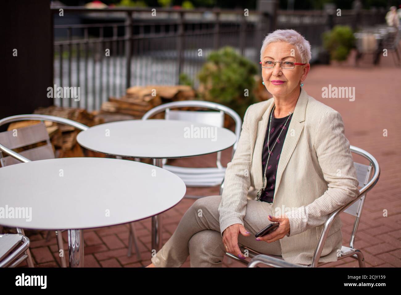 Eine fröhliche Frau, die mit gekreuzten Beinen sitzt, wartet im Café auf Kaffee, Kellner, Freund Stockfoto