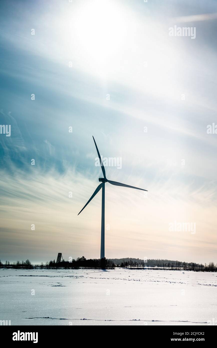 Vertikales Foto von Standalone gestoppt Windmühle, kein Wind. Gefrorene Küste der Ostsee. Große Sonne am Himmel mit weißen blauen rosa Licht Cirrus Wolken. Kalte Sonne Stockfoto