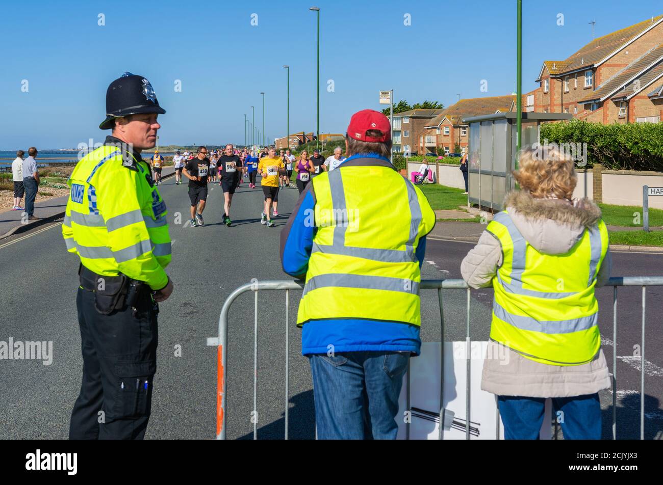 Freiwillige und Polizei, die als Marschalls, Rangieren einer Wohltätigkeitslauf in England, Großbritannien. Community Running Event Marschall. Stockfoto