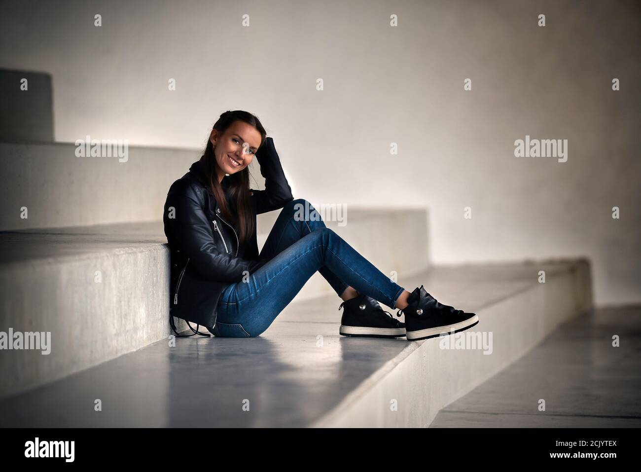 Schönes Modell in stilvoller schwarzer Lederjacke auf der Betontreppe sitzend. Stockfoto