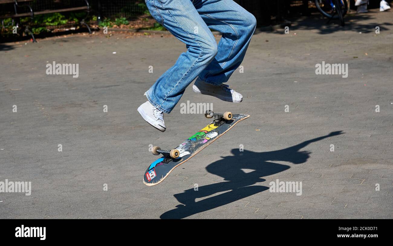 NEW YORK, NY - 8. SEPTEMBER 2020: Skateboarder macht einen Trick im Park. Shot ist ein Detail, zeigt Beine, Brett und Schatten auf dem Bürgersteig Stockfoto