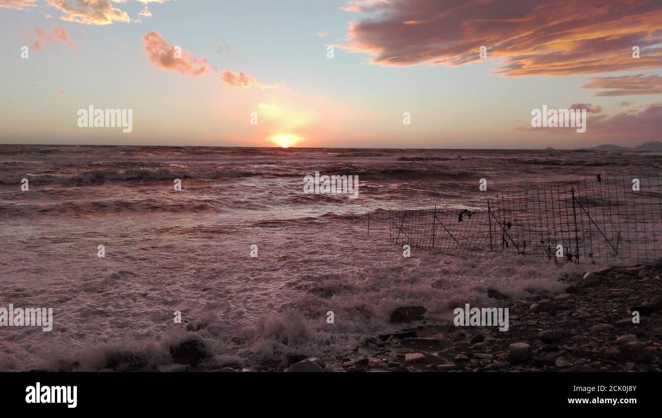 Ein Blick auf den Strand bei Sonnenuntergang, ein magischer Moment, in dem alles mit hellen Farben gefärbt ist. Die Wolken umrahmen die maritime Landschaft und die Stockfoto