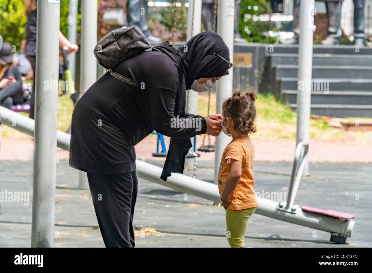 Istanbul/Türkei - 05/20/2020; EINE muslimische Mutter mit schwarzem Schal und Kleidung fixiert die Gesichtsmaske ihrer Tochter auf dem Spielplatz der Kinder. Stockfoto