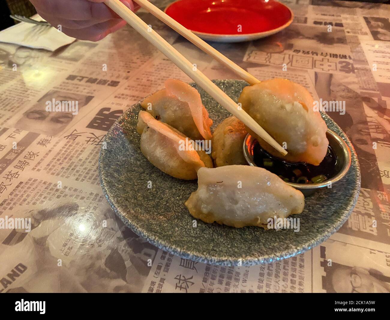 Eine Person, die in einem asiatischen Fusion-Restaurant einen Hühnerknödel mit Essstäbchen in einen kleinen Behälter mit Sauce taucht. Stockfoto