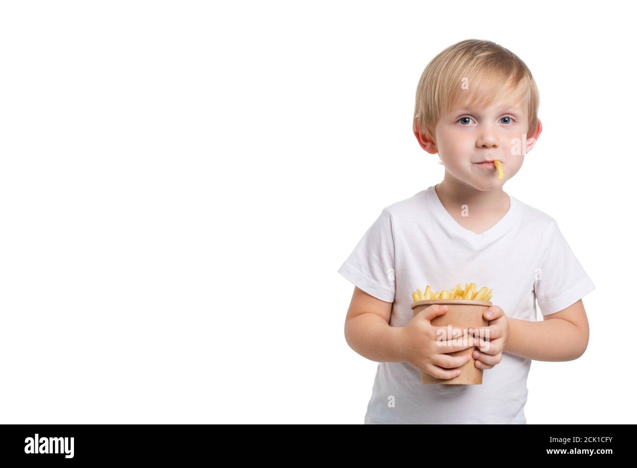 Ein blondes, weißhäutig Kind hält eine Einweg-Tasse Pommes frites und ein Stück Fast Food steht aus seinem Mund. Glücklicher Junge in einem Studio-Aufnahme. Clos Stockfoto