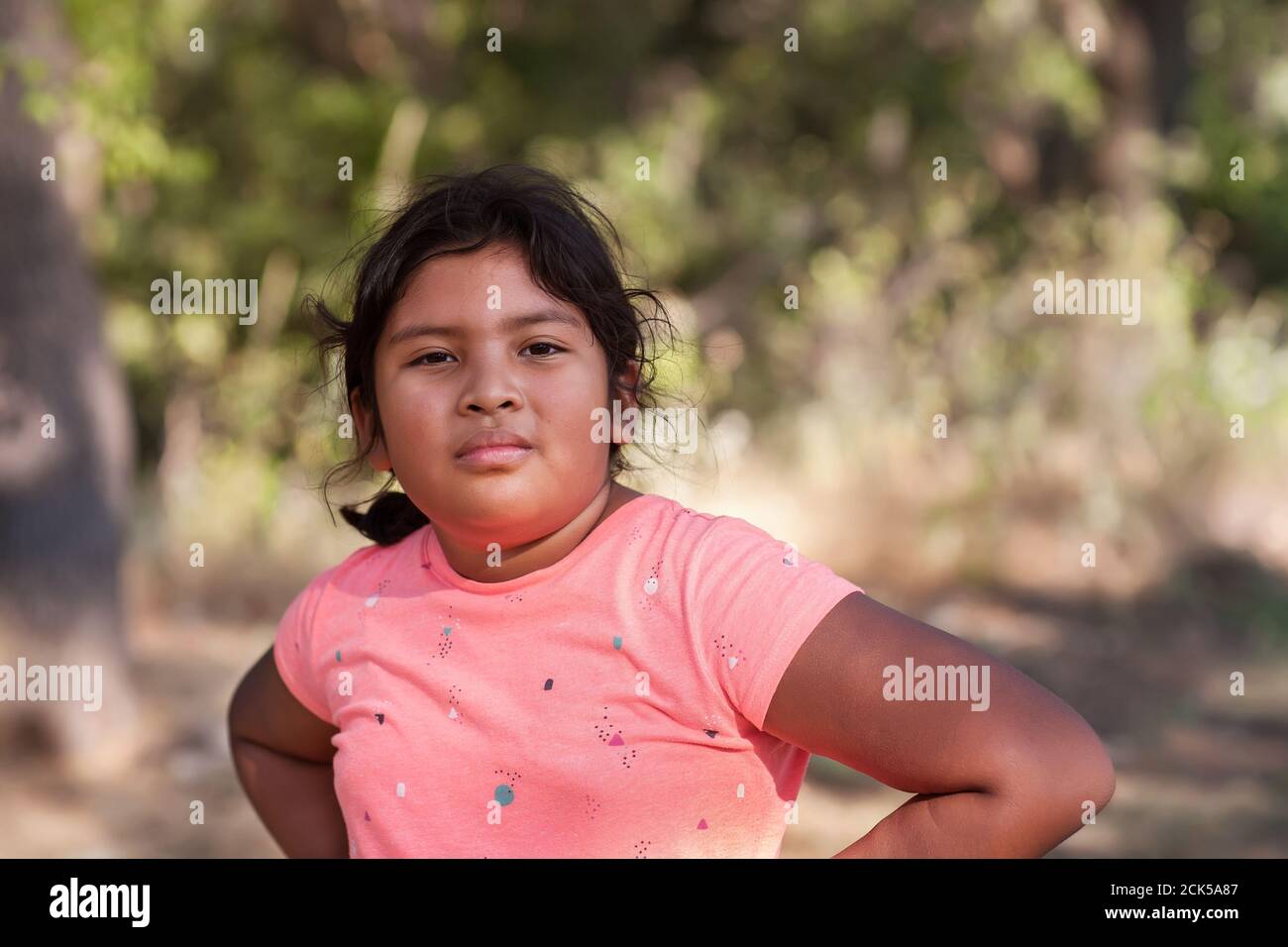 Ein junges Latino-Mädchen mit Armen, die auf ihren Hüften ruhen und eine aggressive Haltung ausdrücken, feindselig oder einschüchternd. Stockfoto