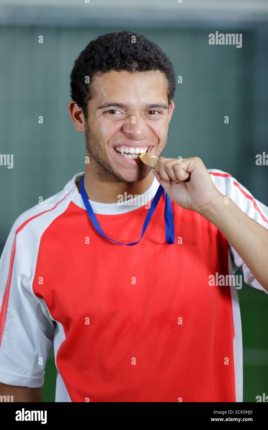 Nahaufnahme eines gutaussehenden jungen Athleten, der seine Medaille beißt Stockfoto