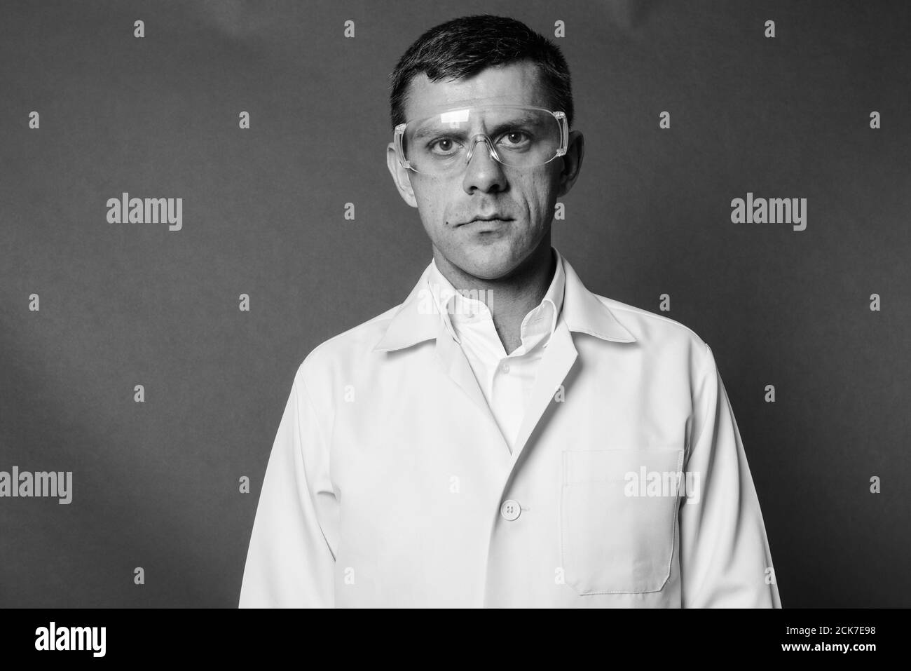 Gutaussehender Arzt mit Schutzbrille vor grauem Hintergrund Stockfoto