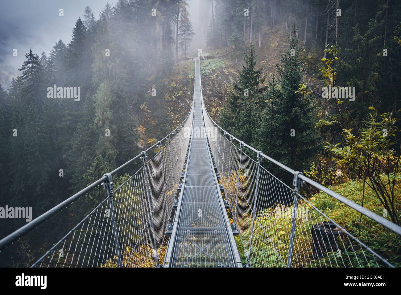 Hängebrücke aus Metall über dem schönen Rabby-Tal im Nebel irgendwo in Norditalien im Frühherbst. Stockfoto