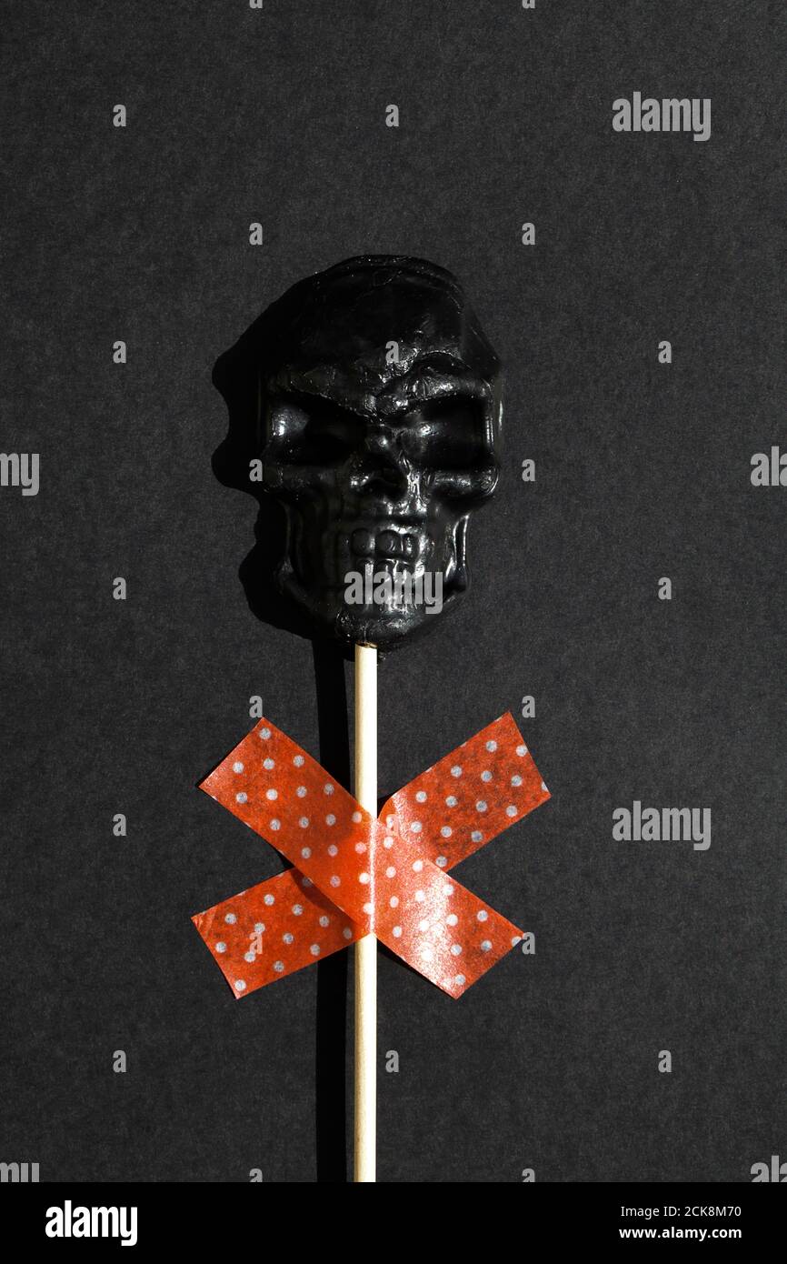 Schwarzer Lollipop in Form von Totenkopf auf schwarzem Hintergrund. Kreative Halloween Minimal Konzept. Flach Lay Draufsicht Stockfoto