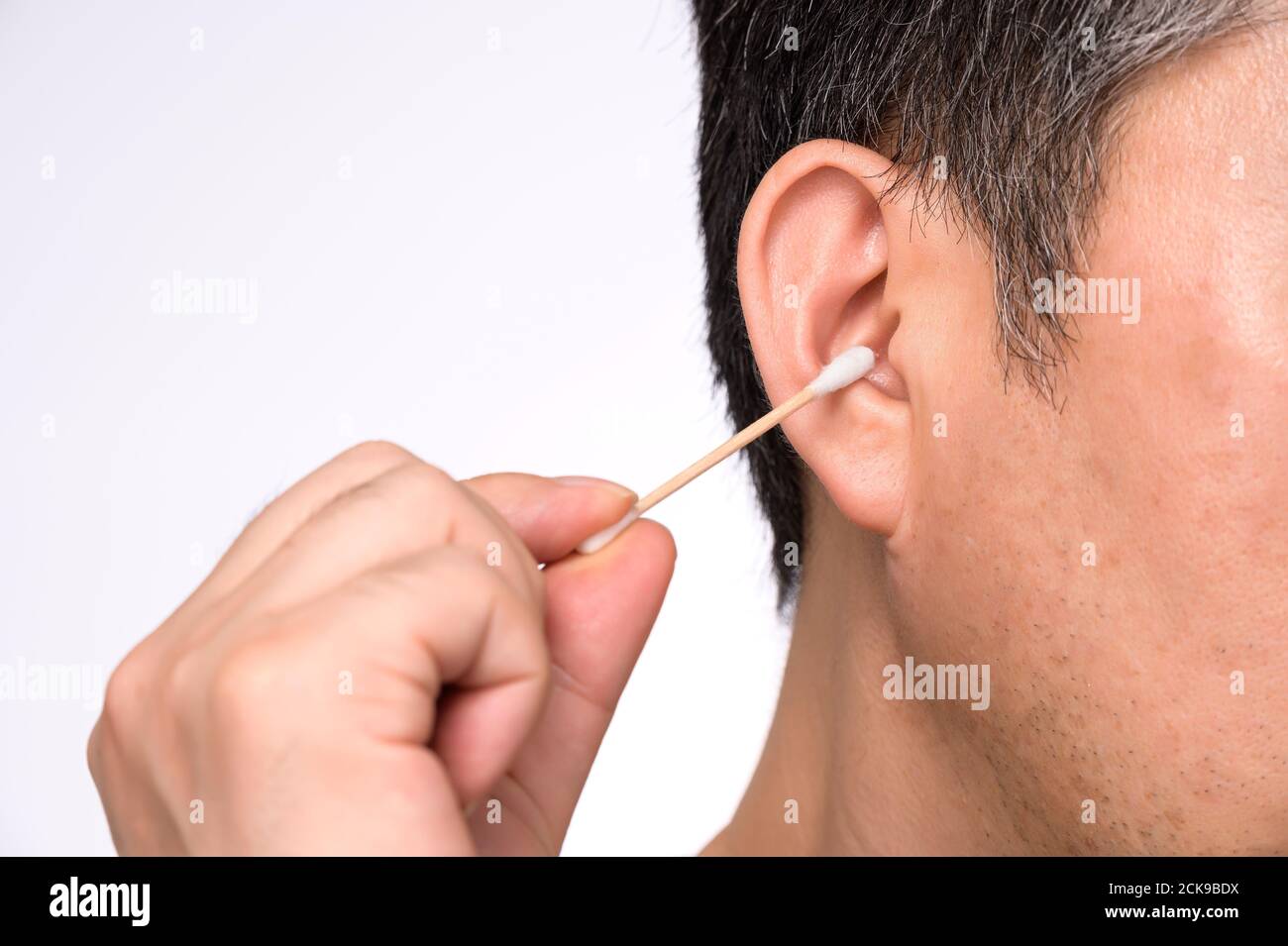 Nahaufnahme eines Mannes mittleren Alters, der seine Ohren mit einem Wattestäbchen abwischt. Stockfoto