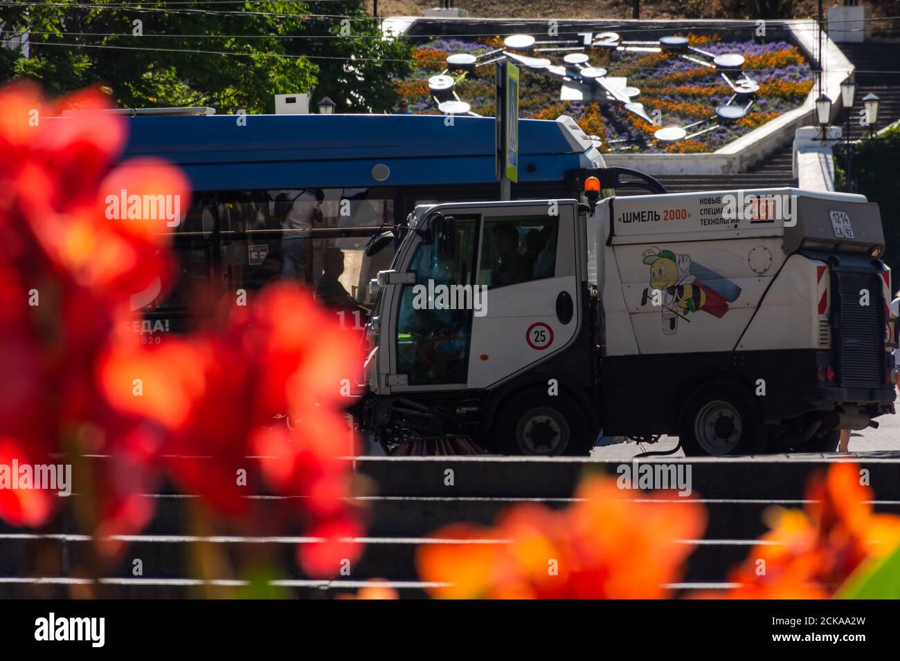 Sewastopol Stadtzentrum mit Menschen und Autos am 13. August 2020. Reinigung der Straße mit einem kleinen Hummel Auto. Bunte Stadtlandschaft. Rote Kannas in A Stockfoto