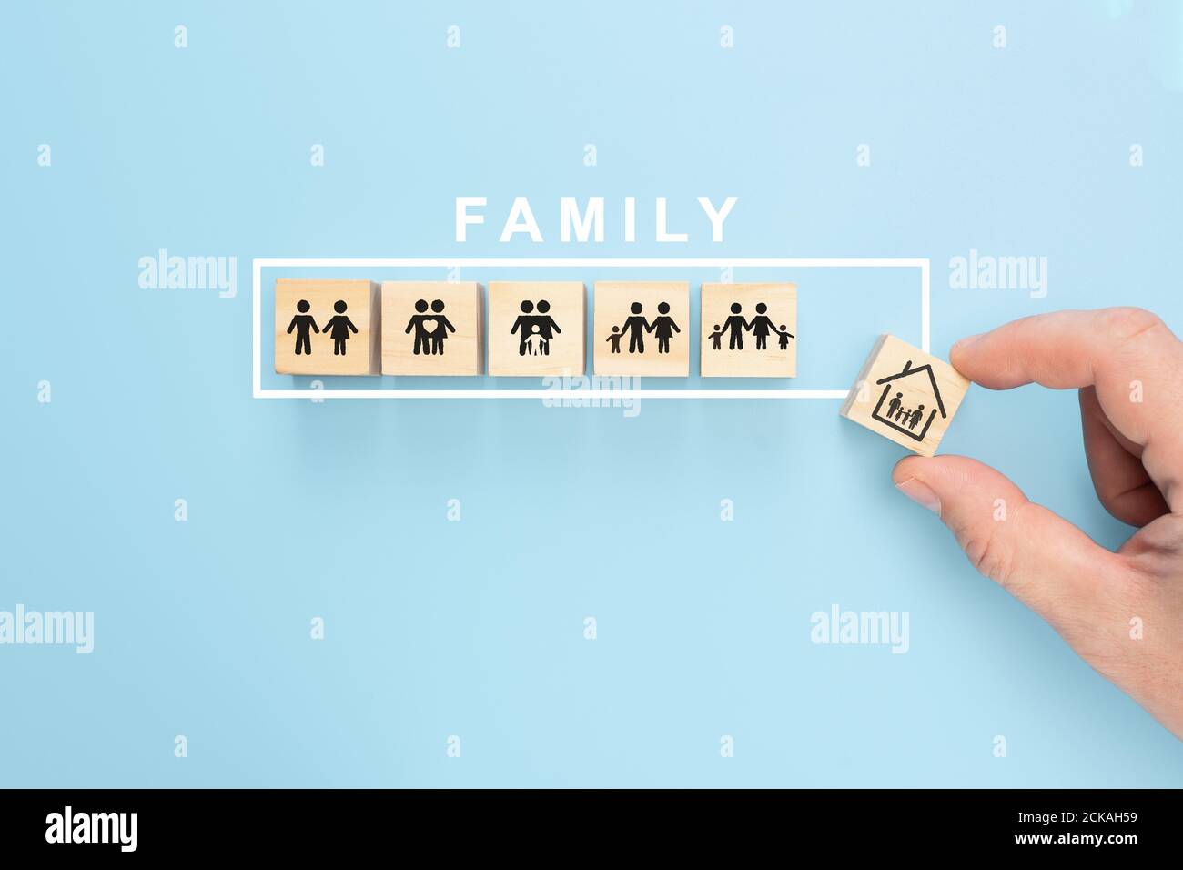 Hand anordnend Holzwürfel mit Familiensymbol auf pastellblauem Hintergrund, Kopierraum. Handgriff Holzblock mit Icon Family Konzept Stockfoto