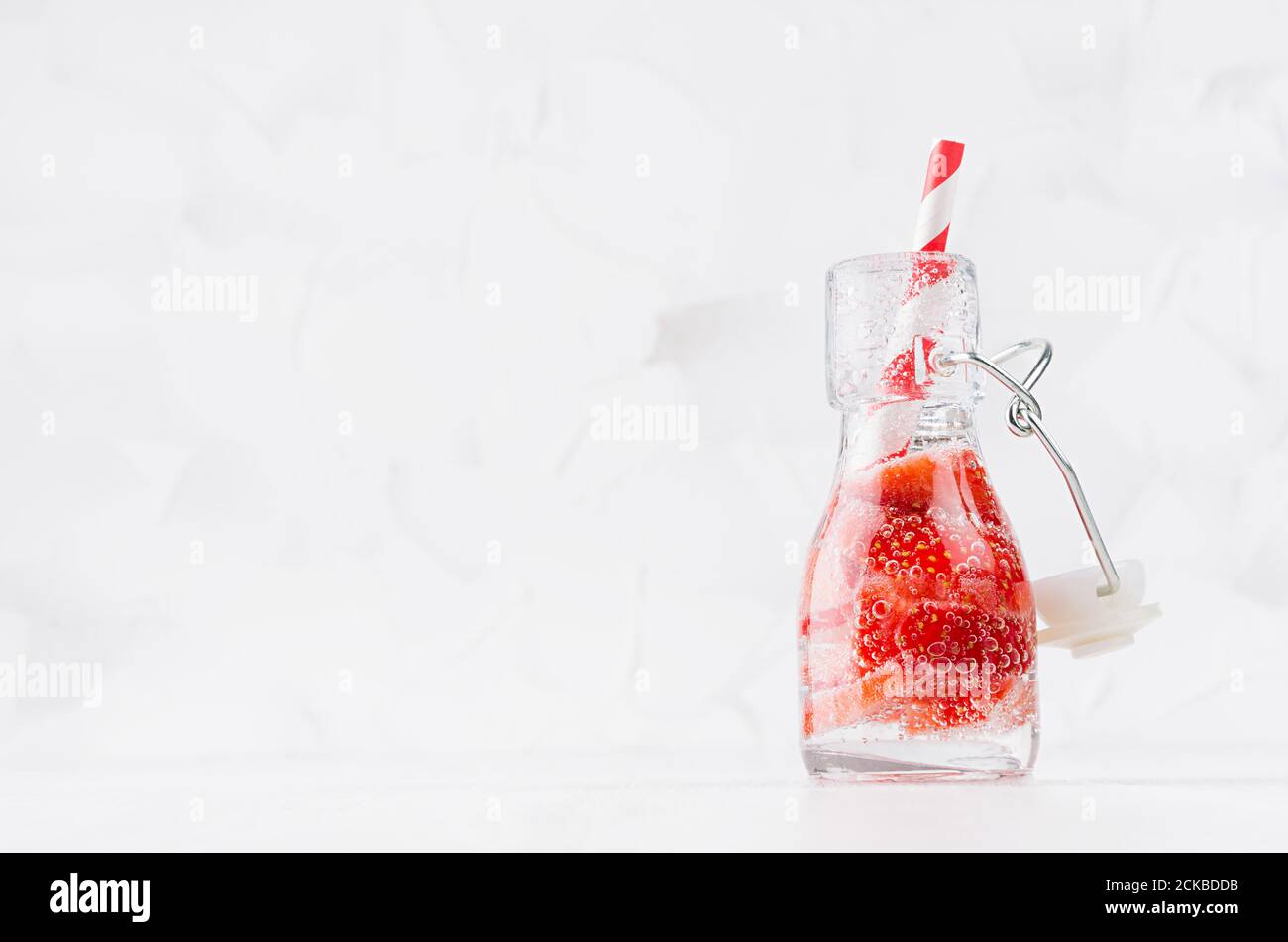Frische Erdbeerlimonade mit geschnittener Beere, Sodawasser, Stroh in transparenter Yoke-Flasche auf weichem hellweißem Holztisch, Kopierraum. Stockfoto