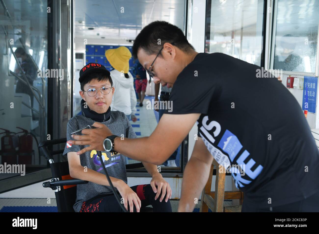 (200916) -- SANYA, 16. September 2020 (Xinhua) -- Fang Jianze schaut zu, wie sein Trainer Luo Min (R) für ihn Tauchausrüstungen in der Nähe der Wuzhizhou Insel in der südchinesischen Provinz Hainan vorbereitet, 29. August 2020. Der 22-jährige Fang Jianze wurde mit EDMD (Emery-Dreifuss Muskeldystrophie) geboren, einer seltenen Muskelerkrankung, die langsam zu Schwäche in den Schultern, Oberarmen und Kälbern führt. Das Leben, das auf einen Rollstuhl beschränkt ist, ist nicht das, was er will. Er will Grenzen überschreiten und weit gehen. Er versuchte Fallschirmspringen im vergangenen Juni und erhielt eine Behindertenzertifizierung Scuba Association in diesem August. In ihm verwirklichte er seinen Tauchtraum Stockfoto