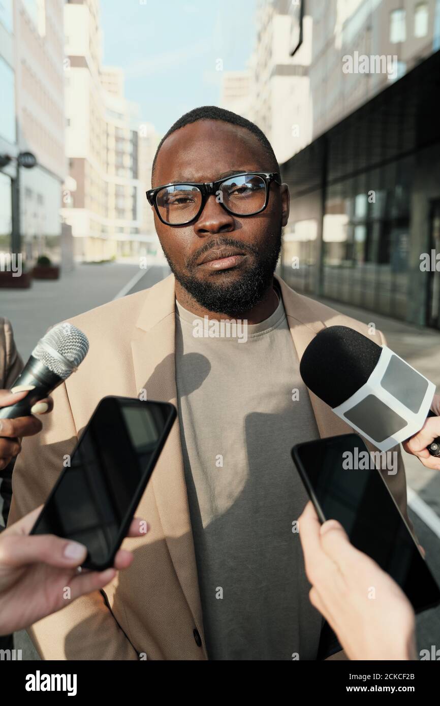 Afrikanischer Geschäftsmann in Brillen im Gespräch mit Journalisten während des Stehens Die Stadt Stockfoto