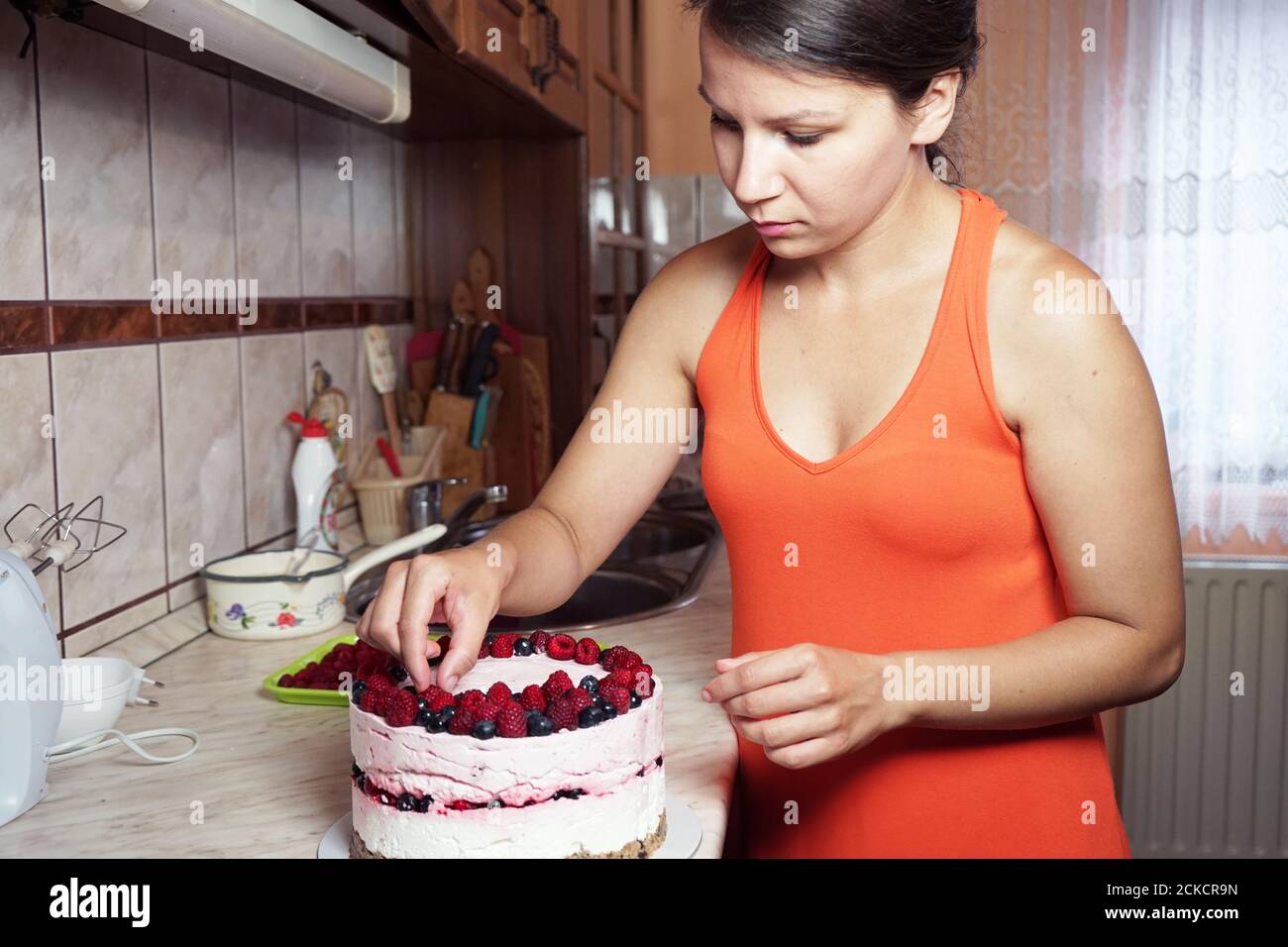 Junge Frau schmückt einen Kuchen in der Küche Stockfoto