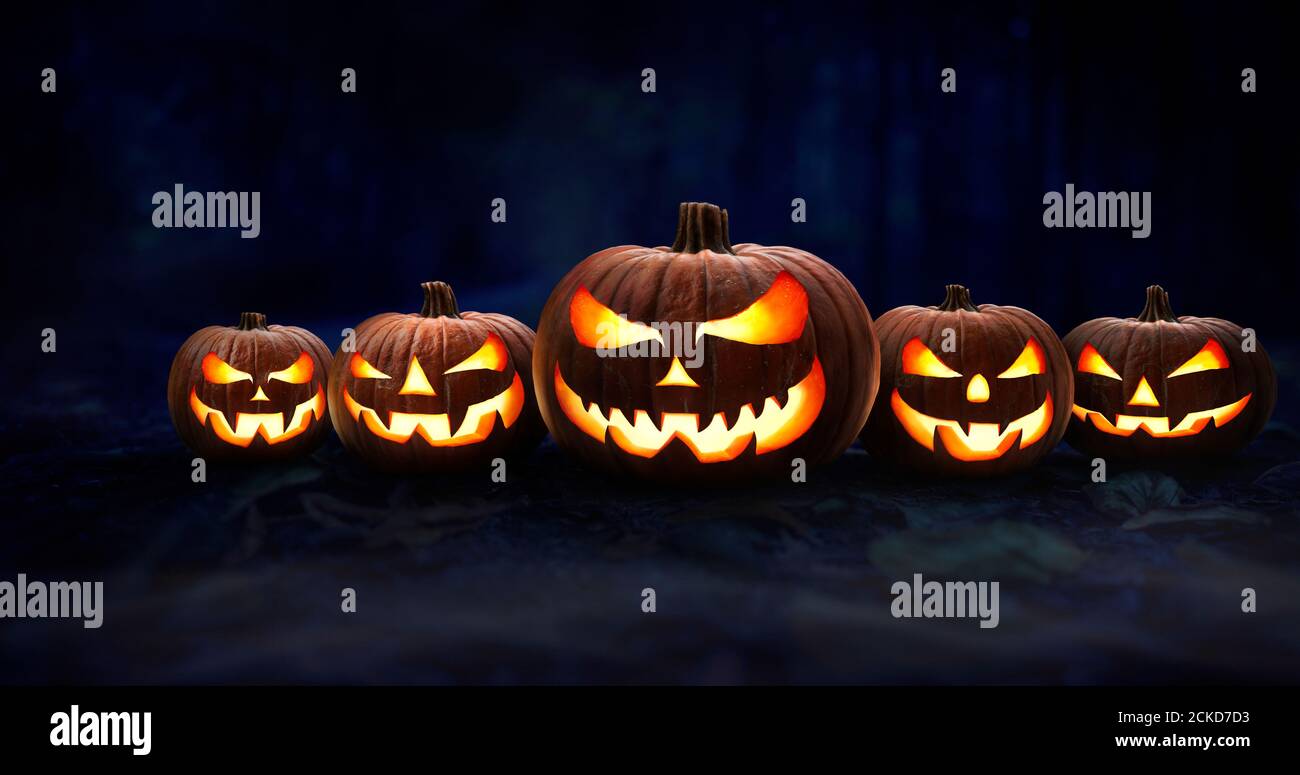 Fünf gruselige halloween Kürbis, Jack O Laterne, mit einem bösen Gesicht und Augen auf dem Waldboden in der Nacht mit einem dunklen Hintergrund. Stockfoto