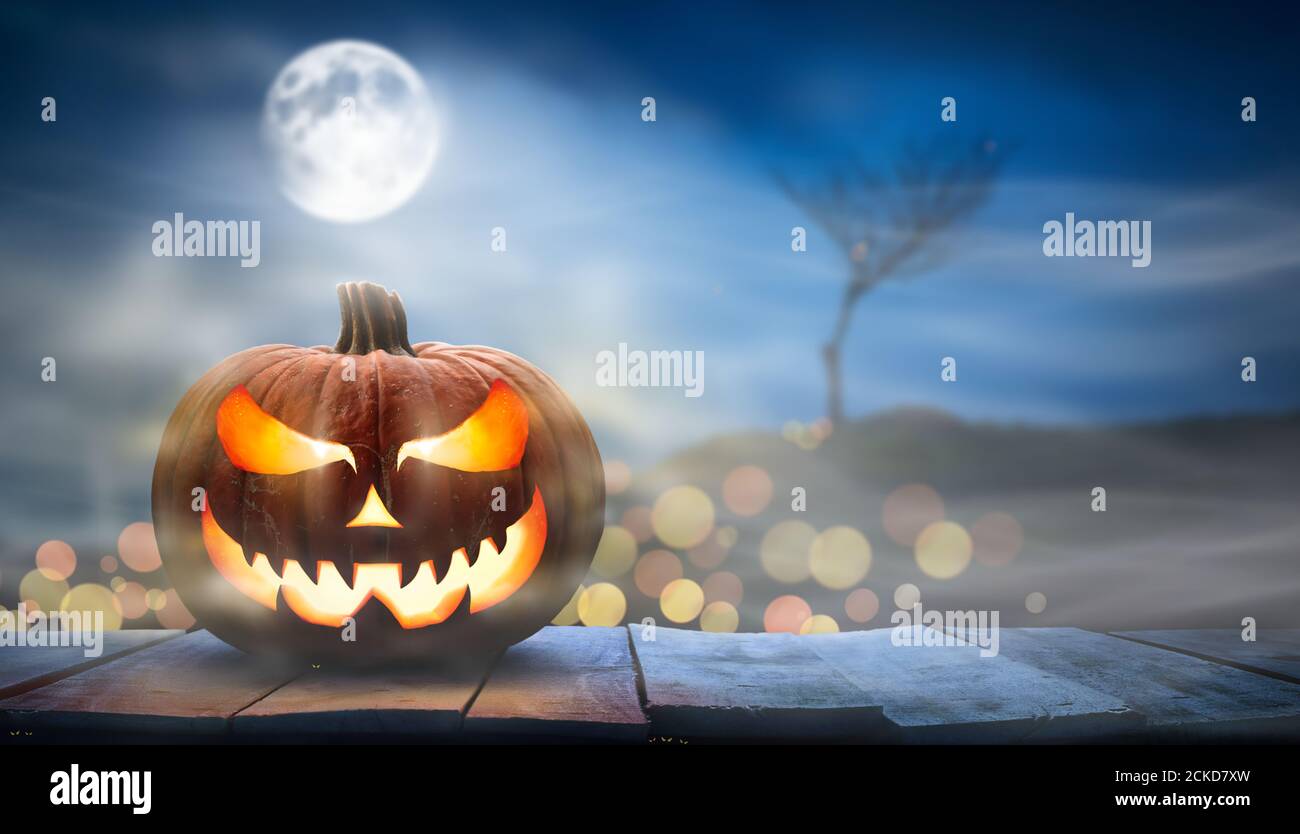 Ein gruseliger halloween Kürbis, Jack O Laterne, mit einem bösen Gesicht und Augen auf einer Holzbank, Tisch mit einem nebligen Nacht Vollmond Hintergrund mit Raum f Stockfoto