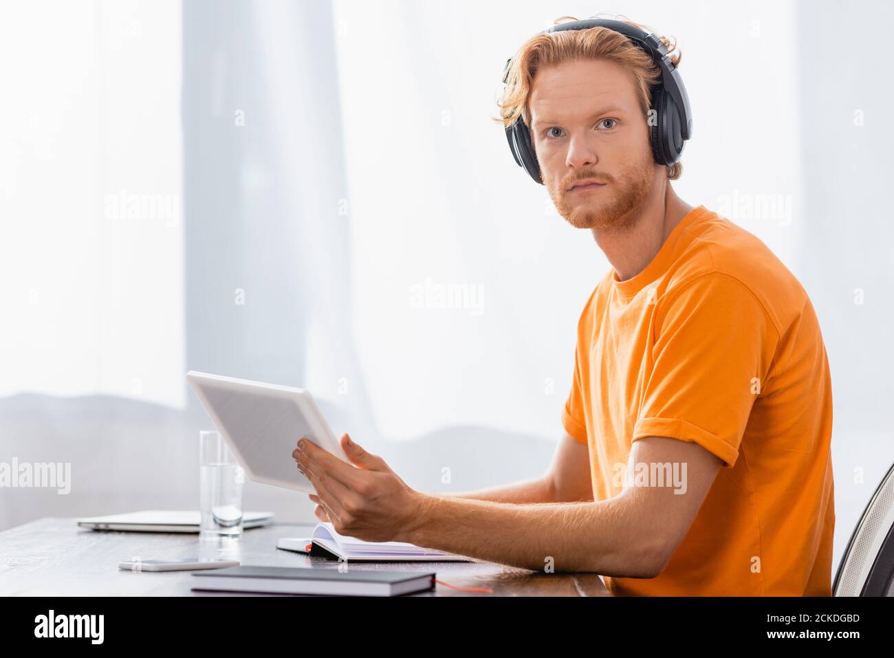 Ein ernsthafter Schüler mit kabellosen Kopfhörern, der ein digitales Tablet hält, während er schaut Bei der Kamera Stockfoto