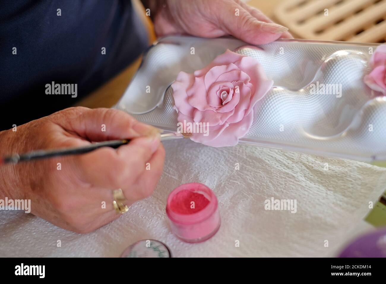 Ältere weibliche Kuchenmacher Malerei rosa vereisten Blütenblätter auf Blume Dekoration Stockfoto