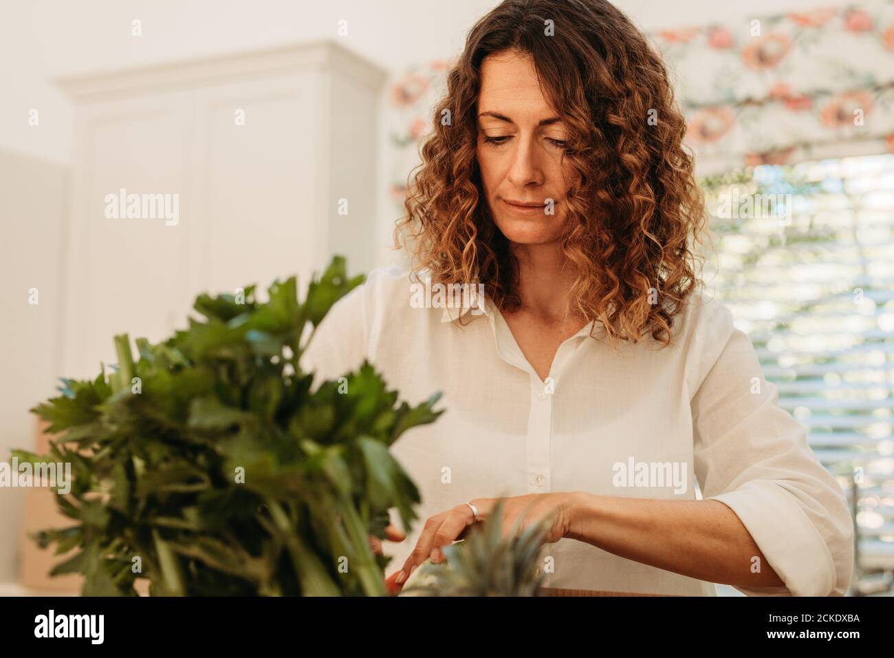 Frau, die das Lebensmittelgeschäft überprüft, das gerade nach Hause geliefert wurde. Weibliche Überprüfung ihrer frischen Gemüse Lieferung in der Küche. Stockfoto