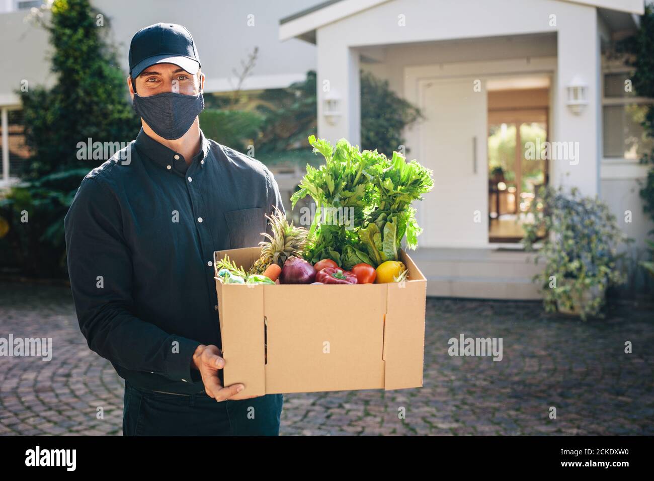 Männlicher Kurierarbeiter liefert Lebensmittel, die während einer Pandemie online bestellt wurden. Person, die eine schützende Gesichtsmaske trägt, liefert Lebensmittel und Lebensmittel. Stockfoto