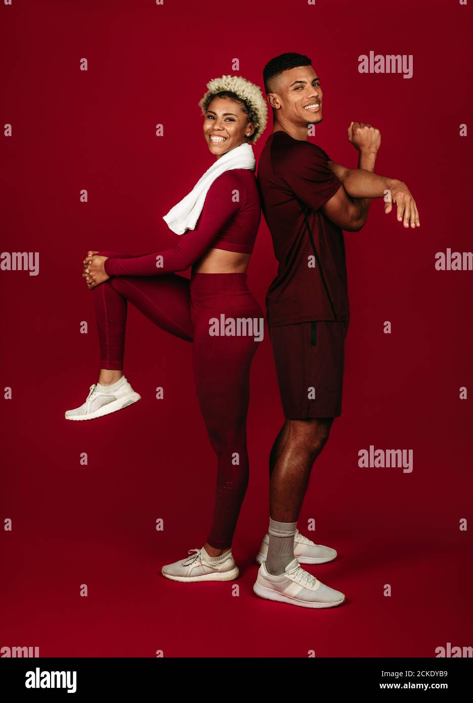 Lächelndes afroamerikanisches Fitness-Paar, das auf kastanienbraunem Hintergrund zusammensteht. Paar macht Aufwärm-Übungen zusammen. Stockfoto