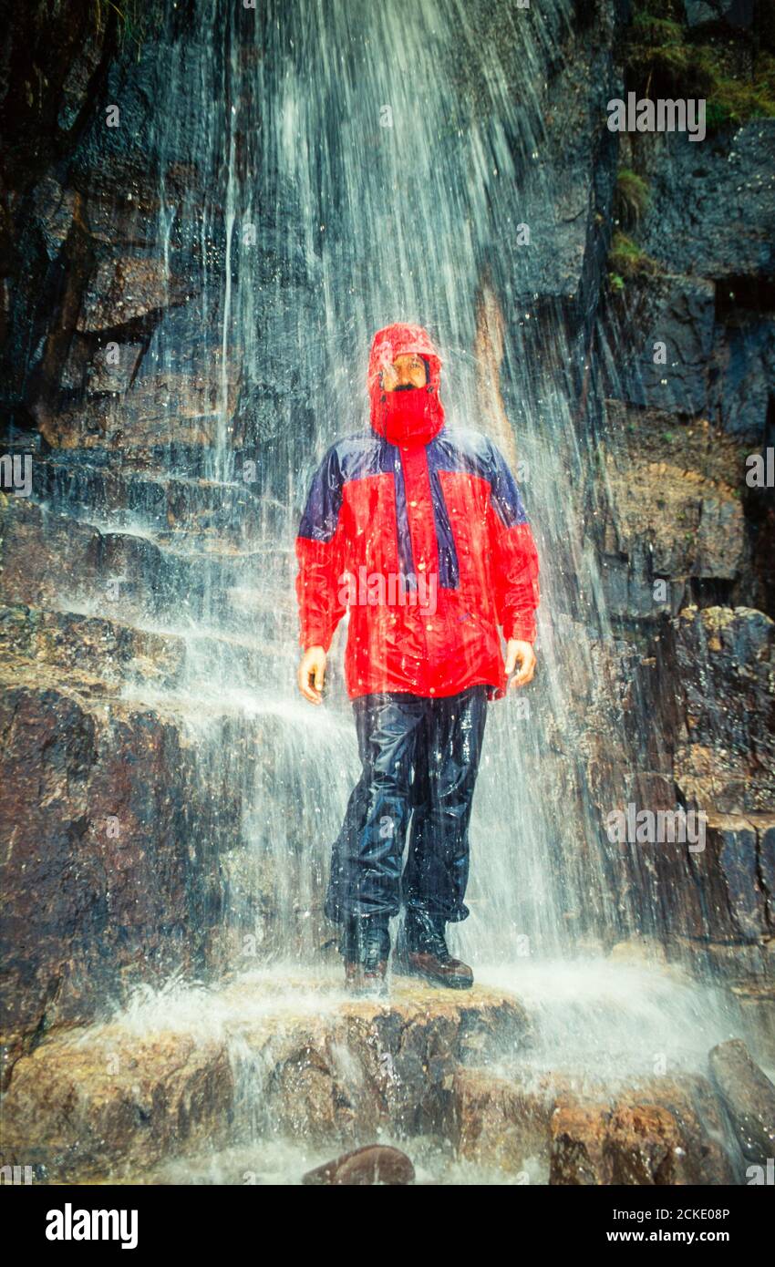Ein Mann mit Wasserproofs stand unter einem Wasserfall, Isle of Mull, Schottland, Großbritannien. Stockfoto
