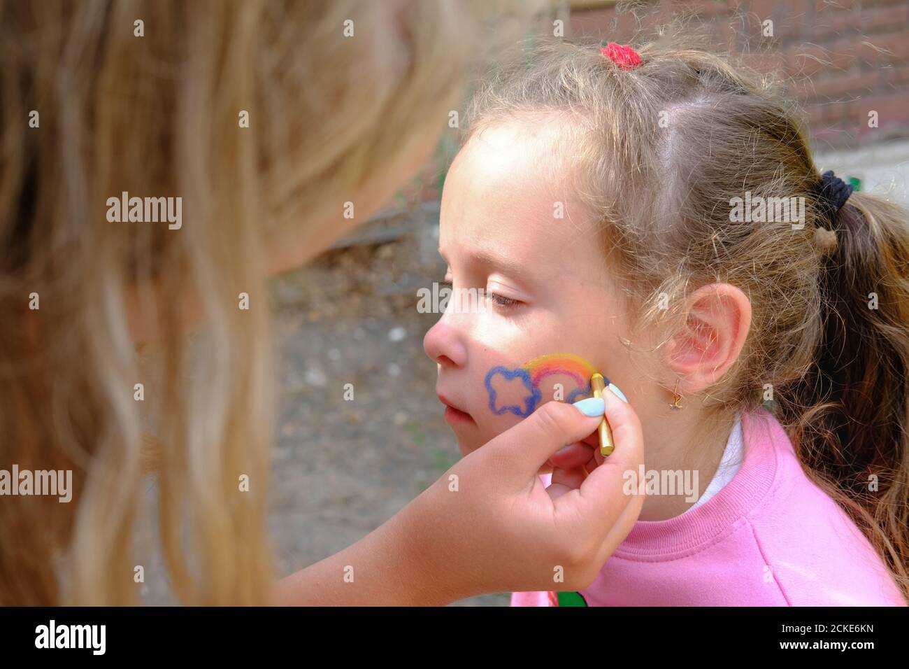 Künstler malen einen Regenbogen auf Mädchen Gesicht. Gesicht sind oder Gesicht malen. Festliche Make-up für Kinder. regenbogen und Wolken auf Babys Wangen. Covid-19 Quarantäne zu Hause. Bleiben Sie zu Hause Medienkampagne Stockfoto