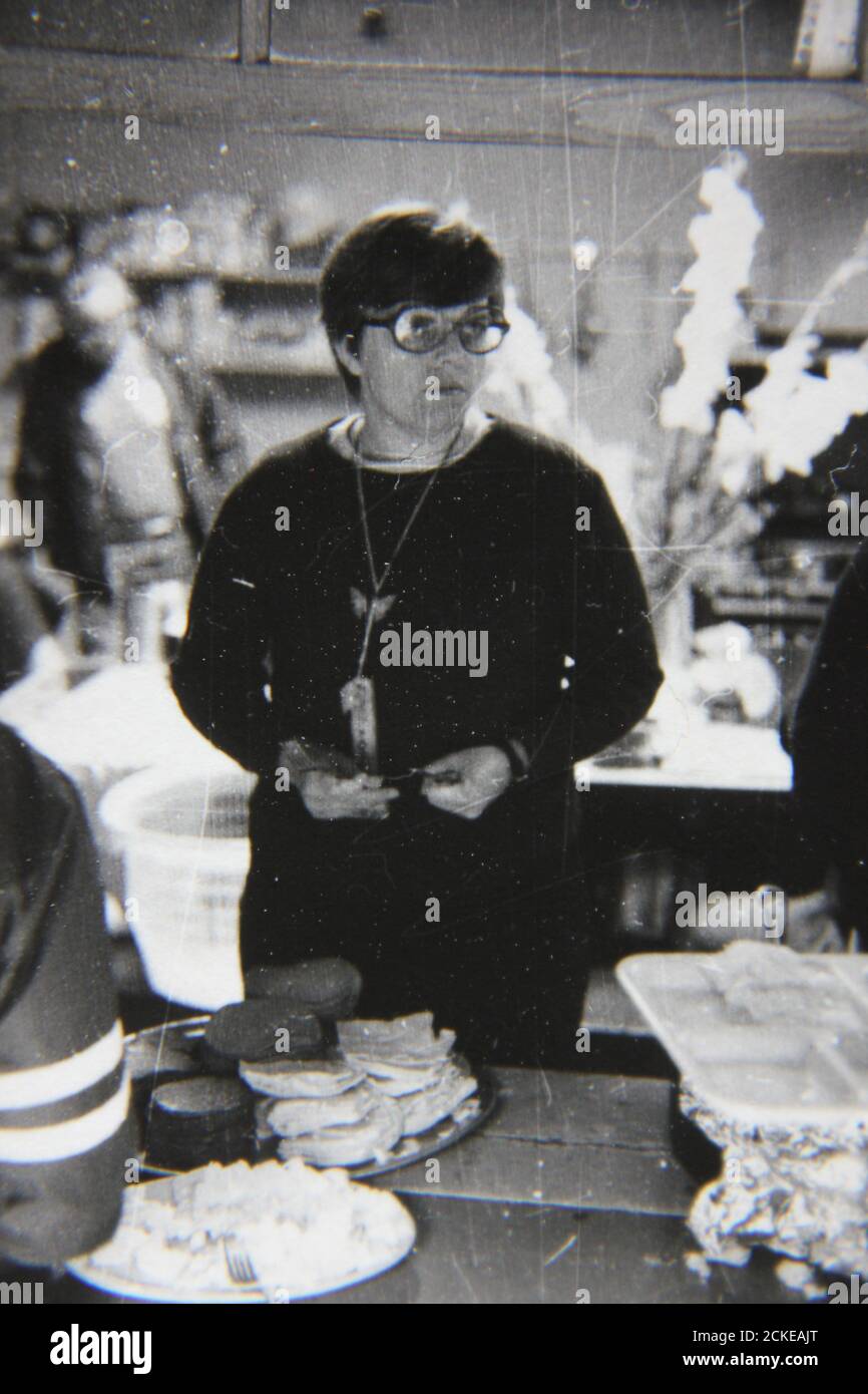 Feine 70er Jahre Vintage Schwarz-Weiß-Fotografie einer Frau, die beim Kochen in der Lagerküche hilft. Stockfoto