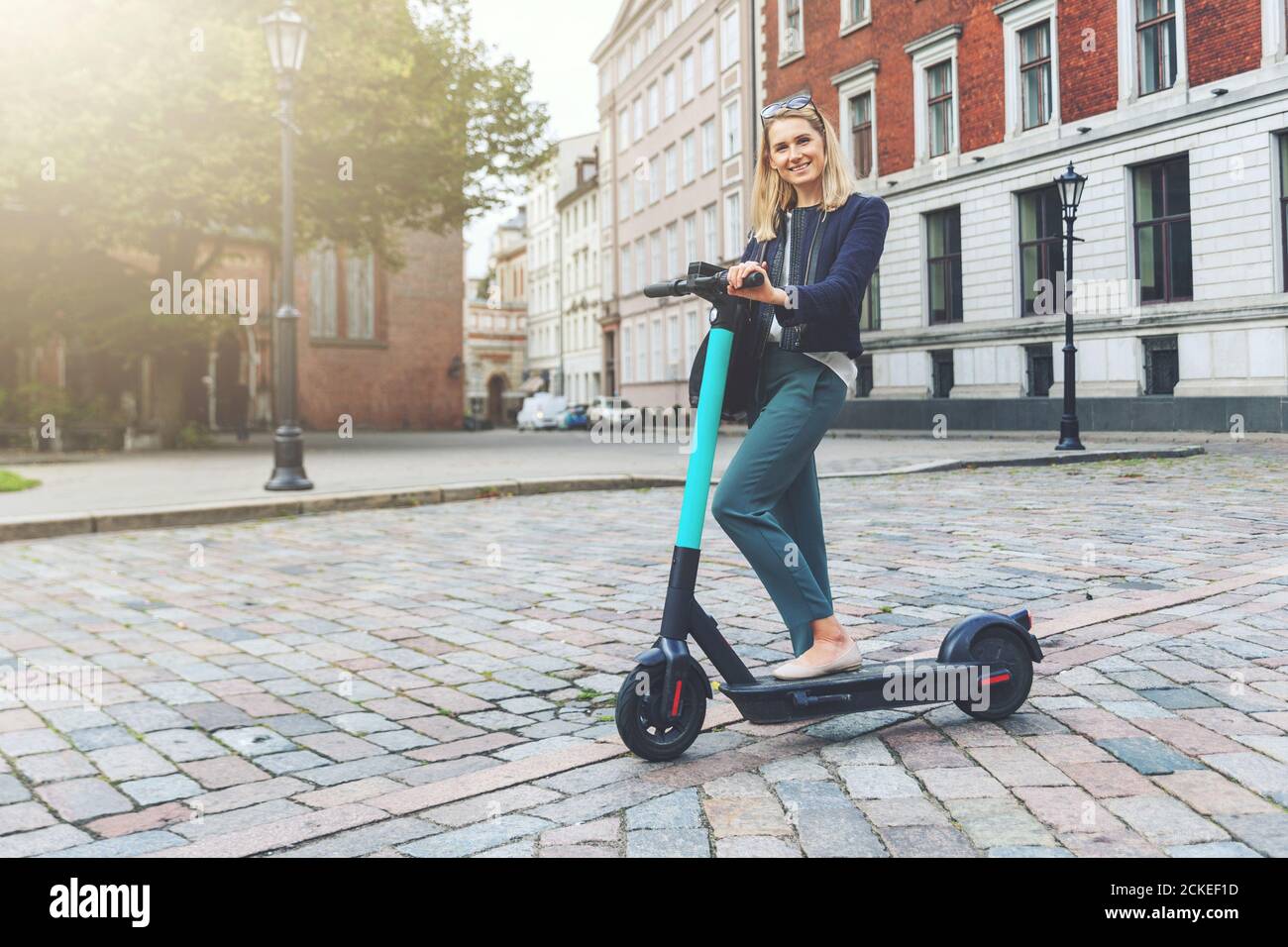 Umweltfreundlicher Transport - junge und schöne Geschäftsfrau fährt Elektroroller in den Straßen der Stadt Stockfoto