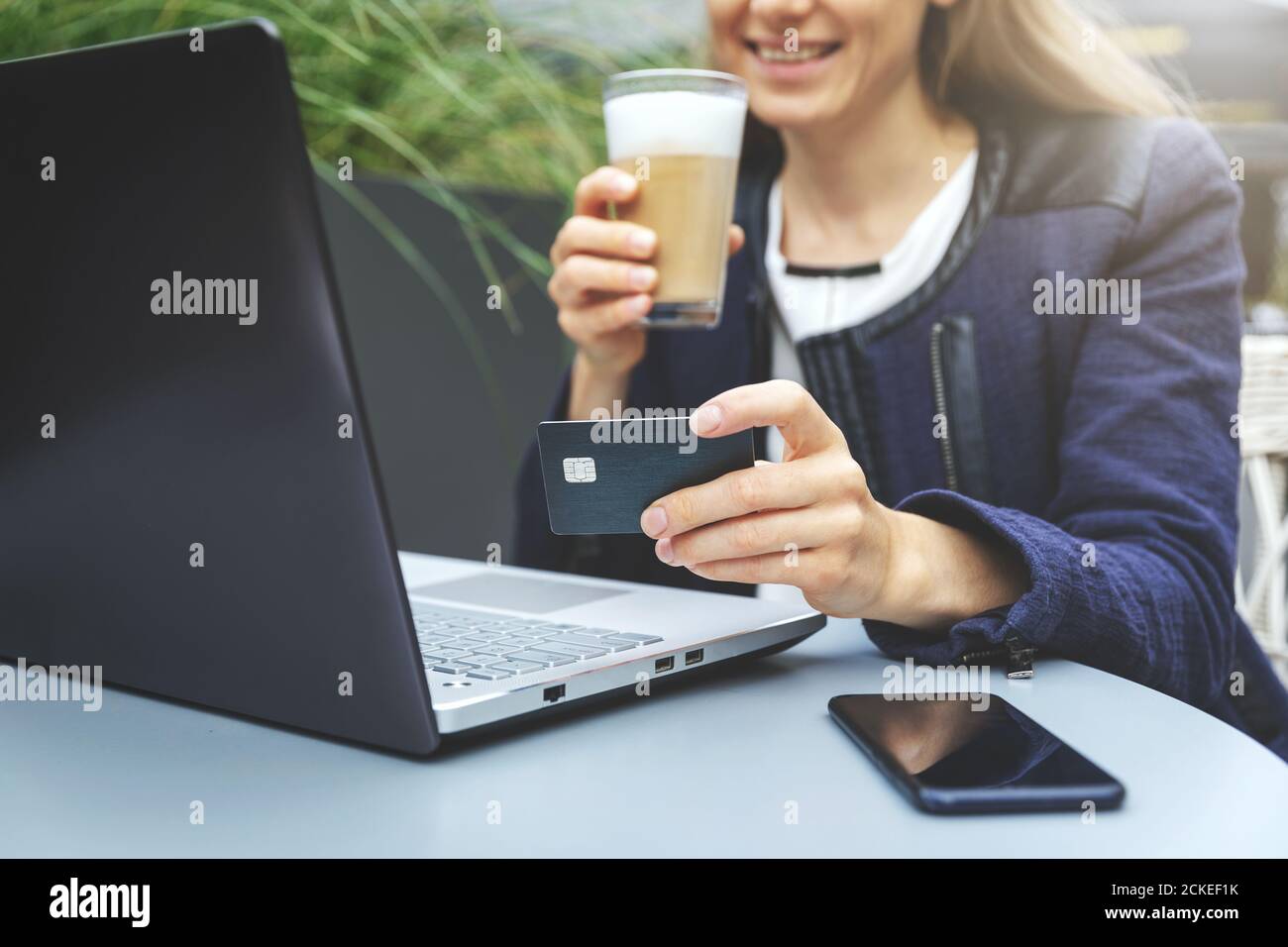 Lächelnde Frau hält Kreditkarte in der Hand und mit Laptop, während Kaffee trinken im Café. Online-Shopping und Zahlungskonzept Stockfoto