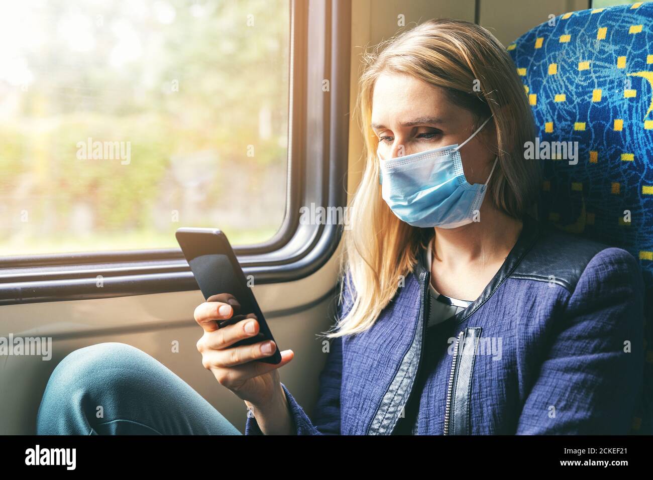 Junge Frau mit Gesichtsmaske mit Handy im Zug. Sicherheit im öffentlichen Verkehr Stockfoto