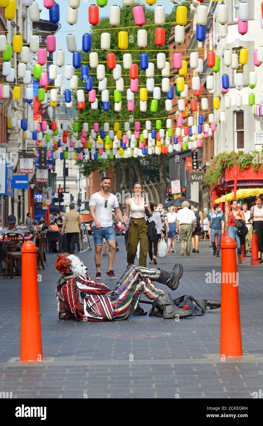 London, England, Großbritannien. Ein Clown (Straßenunterhalter) liegt auf dem Boden in der Wardour Street, Chinatown Stockfoto