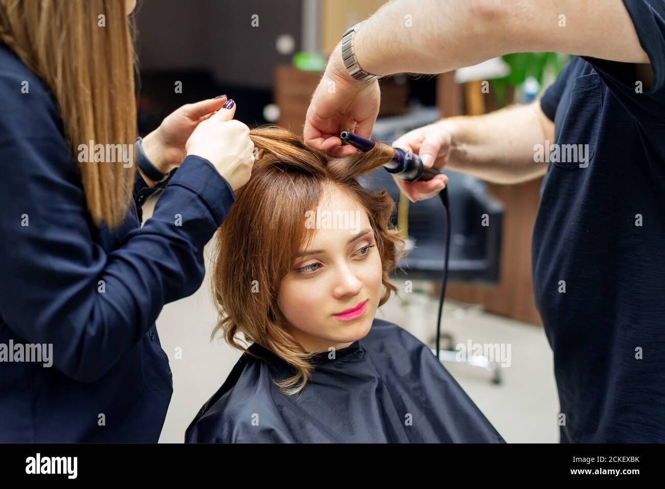Professionelle Friseur dreht Locken von langen hellbraunen Haar der Frau  mit Lockenstab im Schönheitssalon. Friseurverfahren Stockfotografie - Alamy