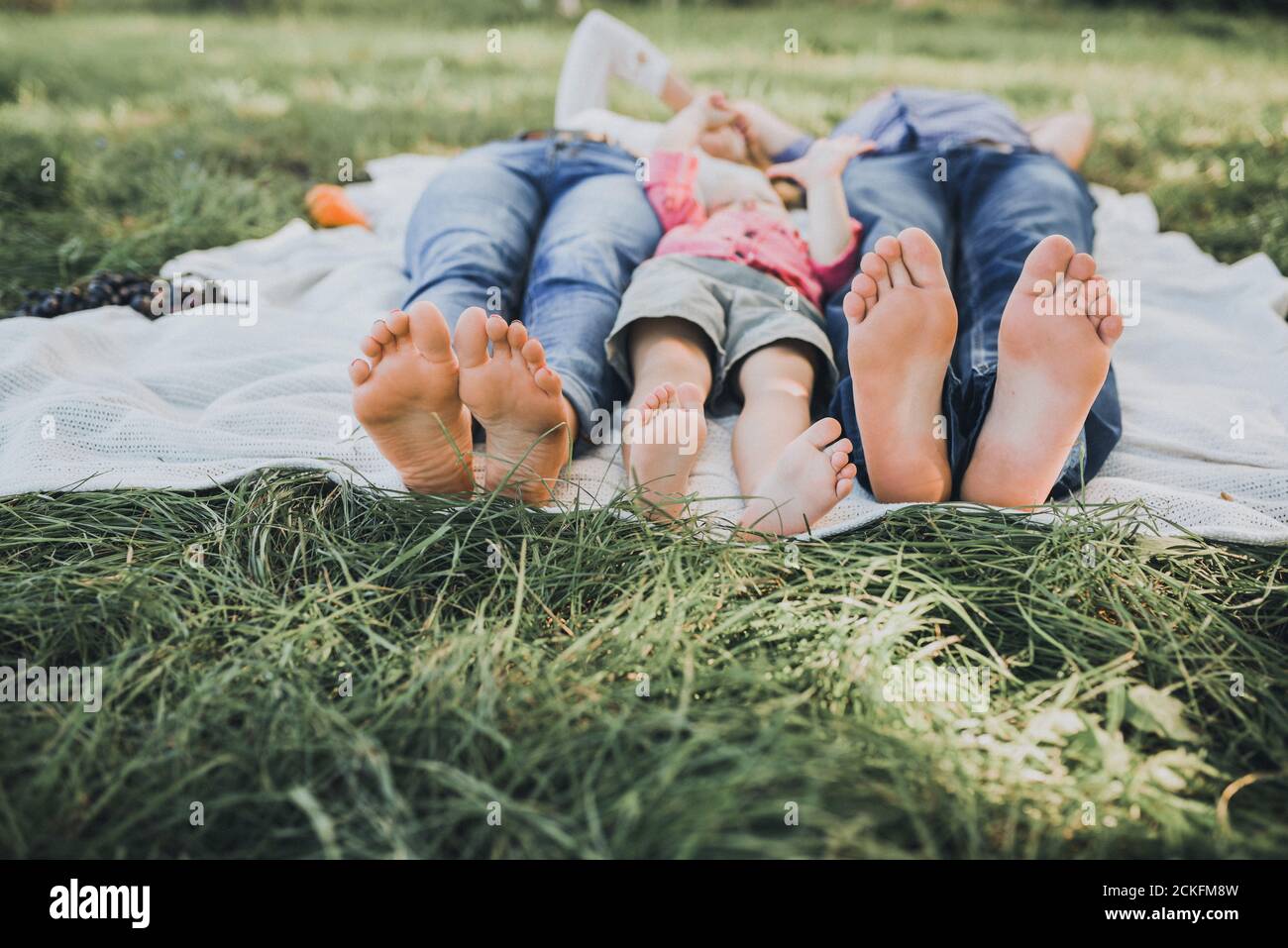 Füße eines Jungen, einer Mutter und eines Vaters. Legen Sie sich auf eine weiße Tagesdecke Stockfoto