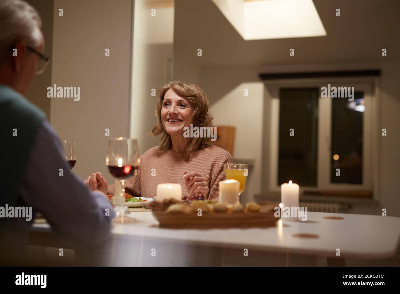 Glückliche ältere Frau, die am Tisch sitzt und mit ihr spricht Ihr Mann beim Abendessen zu Hause Stockfoto